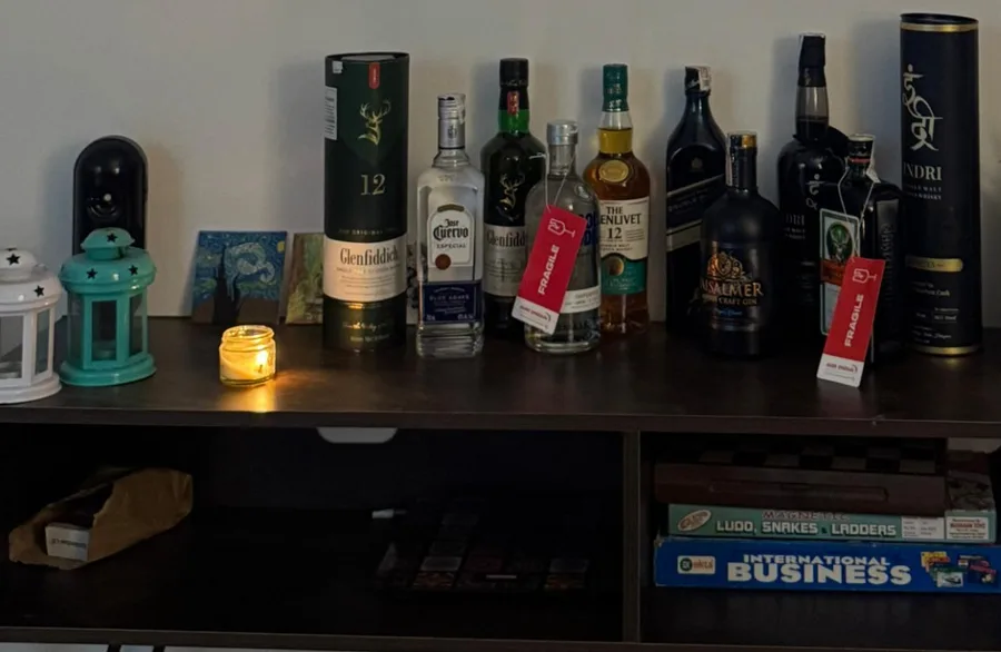 The home bar: a TV unit lined with bottles including Glenfiddich, Jose Cuervo, The Glenlivet, Jaisalmer gin, Jagermeister and Indri, with board games on the shelf below
